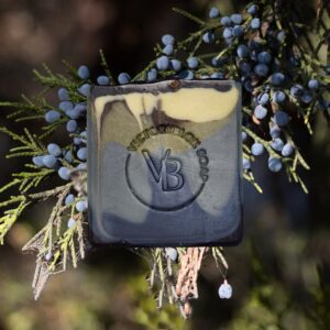 Earth Breath natural clay soap bar with marbled charcoal, green, and blue swirls surrounded by juniper berries.