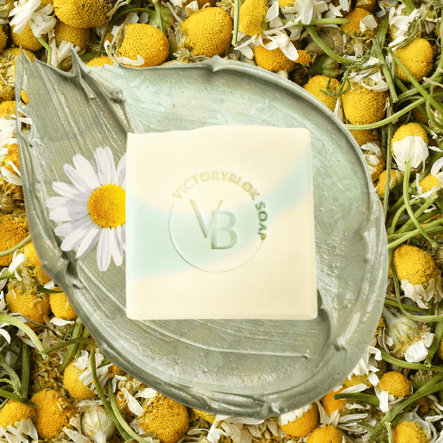 VICTORYBLOKS CHAMOMILE COTTAGE soap bar in soft light green, set against a background of chamomile flowers and a blue sky. Made with olive oil, coconut oil, French green clay, and chamomile essential oil.