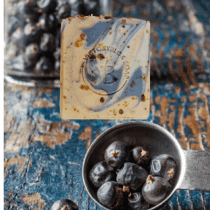 VICTORYBLOK BLACKTHORN JUNIPER Soap Bar with vibrant swirls of color, inspired by juniper berries, displayed beside a stainless steel bowl of fresh juniper berries. Crafted with olive oil, coconut oil, orange and brown clays, indigo powder, juniper and cinnamon essential oils.