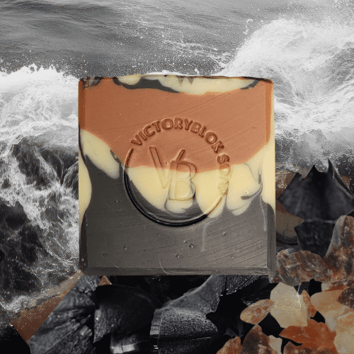 VICTORYBLOKS Frankincense Wildwood soap bar with bold layers of black activated charcoal, cream, and red clay, standing on charcoal and frankincense, set against grey sea waves. Made with olive oil, coconut oil, red clay, activated charcoal, and frankincense essential oil for a soft, foamy, earth-healing cleanse.